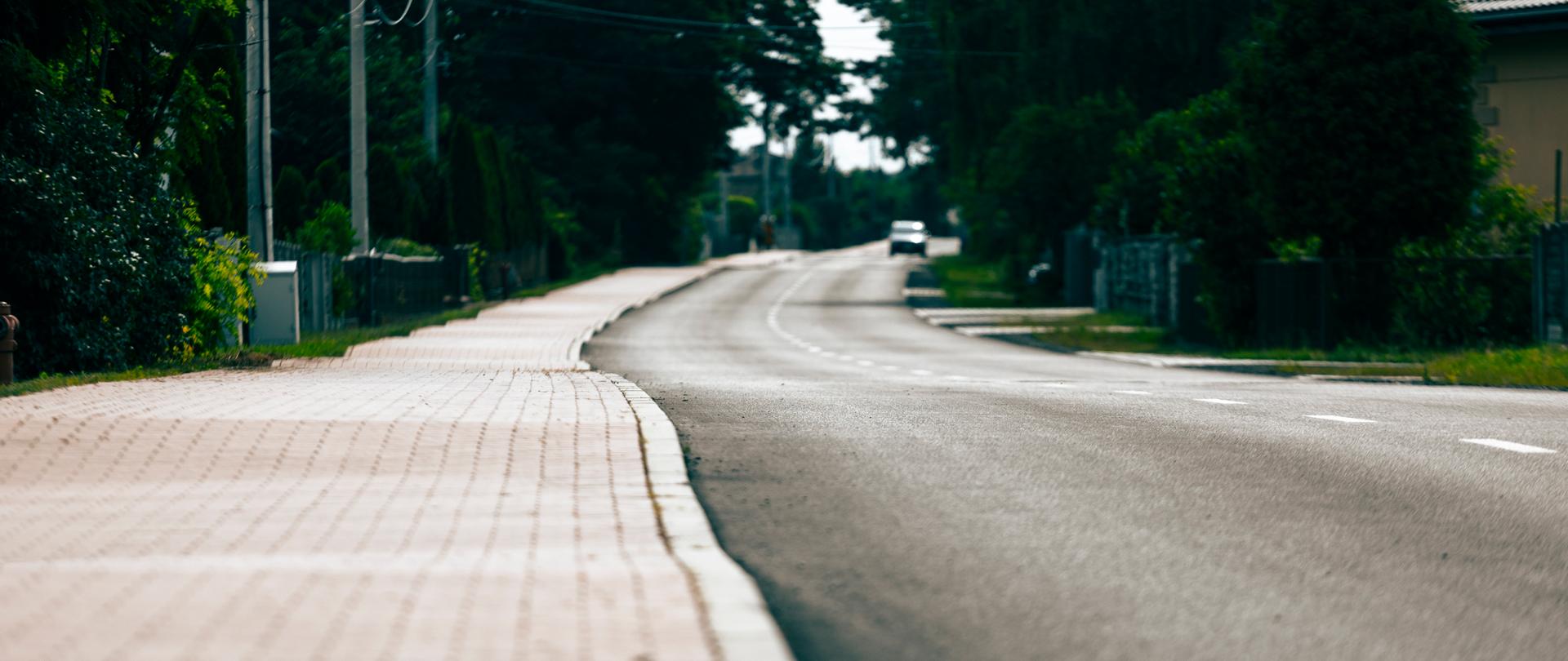 kawałek nowo otwartej drogi oraz chodnika, w oddali widać jadący samochód