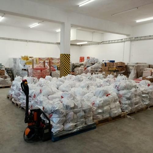 Wnętrze magazynu wypełnionego paczkami ułożonymi na drewnianych paletach.