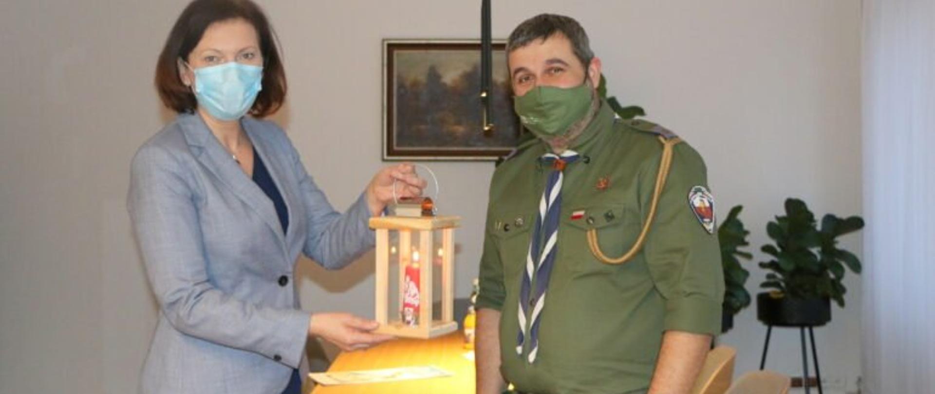Wojewoda podkarpacki Ewa Leniart trzyma drewnianą latarenkę z Betlejemskim Światłem Pokoju. Obok niej stoi komendant Chorągwi Podkarpackiej Związku Harcerstwa Polskiego Mariusz Bezdzietny. 