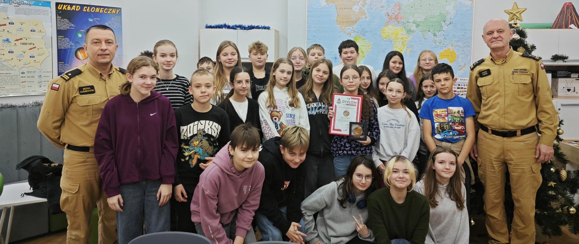 Pamiątkowe zdjęcie wykonane po wręczeniu młodej bohaterce odznaki "Iuvenis Forti". Na zdjęciu przedstawiciele Komendy Powiatowej PSP w Pabianicach oraz klasa młodej bohaterki.