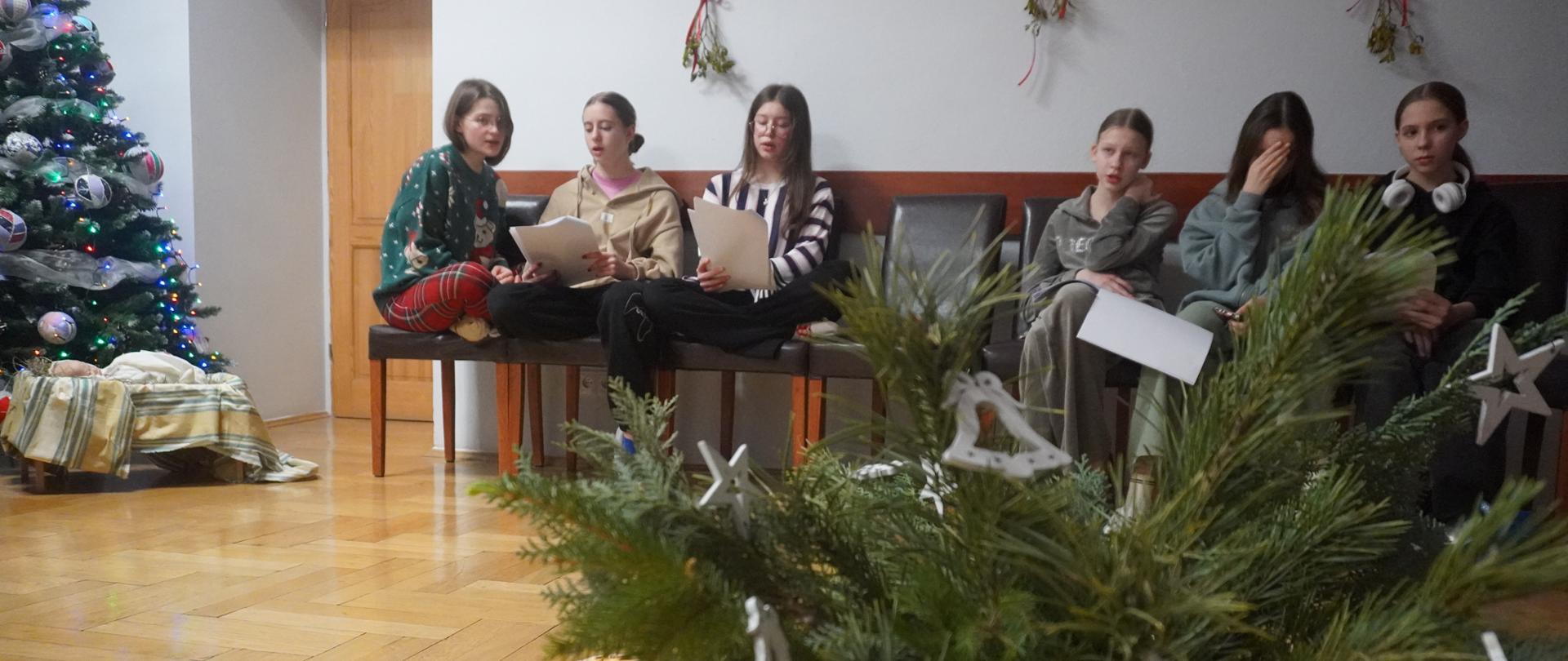 Wychowankowie zebrali się w świetlicy. W świątecznej atmosferze, przy choince i stroiku wykonują kolędy i pastorałki. 