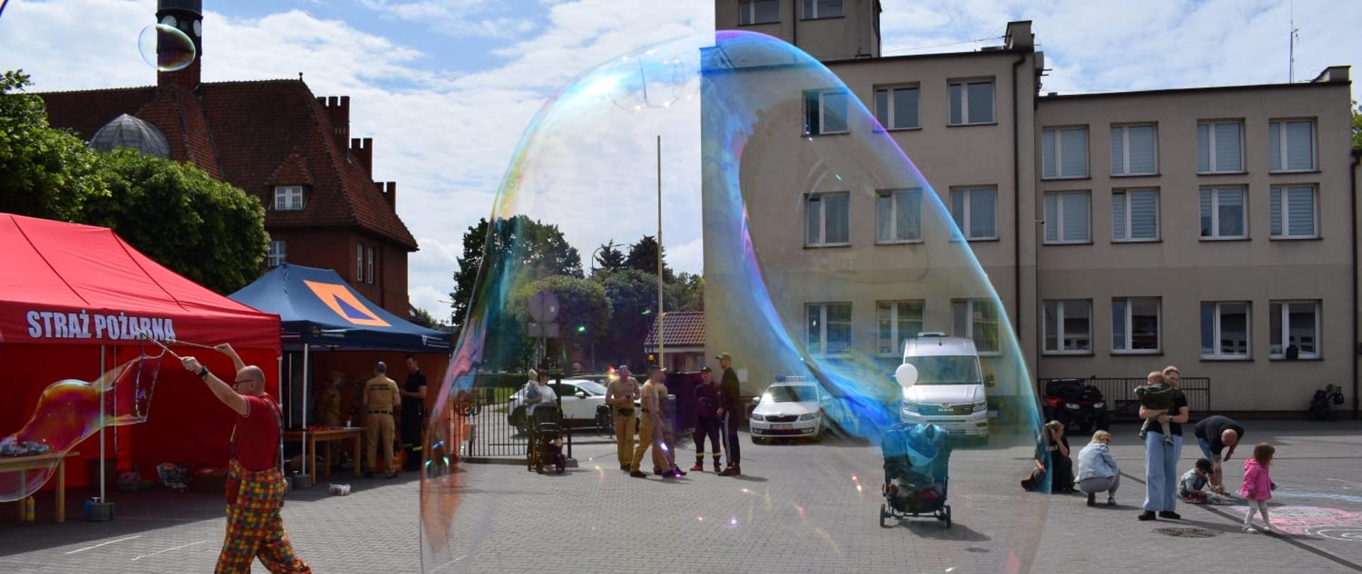 Zdjęcie placu JRG, na pierwszym planie bańka mydlana, przez nią widać komendę i namioty straż