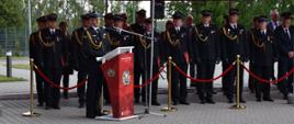 Przemówienie w trakcie uroczystości, na drugim planie zgromadzeni goście. W tle budynek komendy.