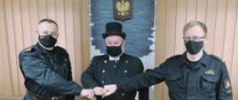 Dwóch strażaków stoi z kominiarzem. Wszyscy ubrani na czarno.