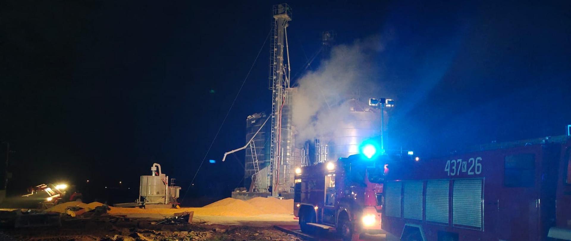 Na zdjęciu widać pożar suszarni , oraz nieobjęte pożarem silosy z kukurydzą, obok pojazdy gaśnicze PSP i OSP.