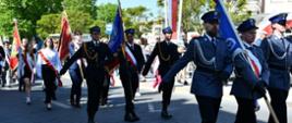 Zdjęcie przedstawia poczty sztandarowe w trakcie przemarszu. Od prawej strony poczet Policji, następnie Państwowej Straży Pożarnej oraz poczty towarzyszące.
