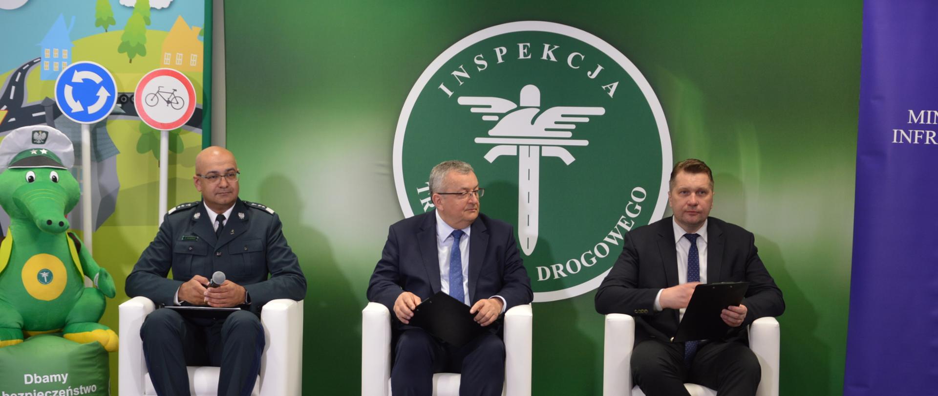 Od lewej siedzą Alvin Gajadhur, Główny Inspektor Transportu Drogowego, Andrzej Adamczyk, Minister Infrastruktury oraz minister Przemysław Czarnek. Za nimi znajduje się logo Inspekcji Transportu Drogowego.