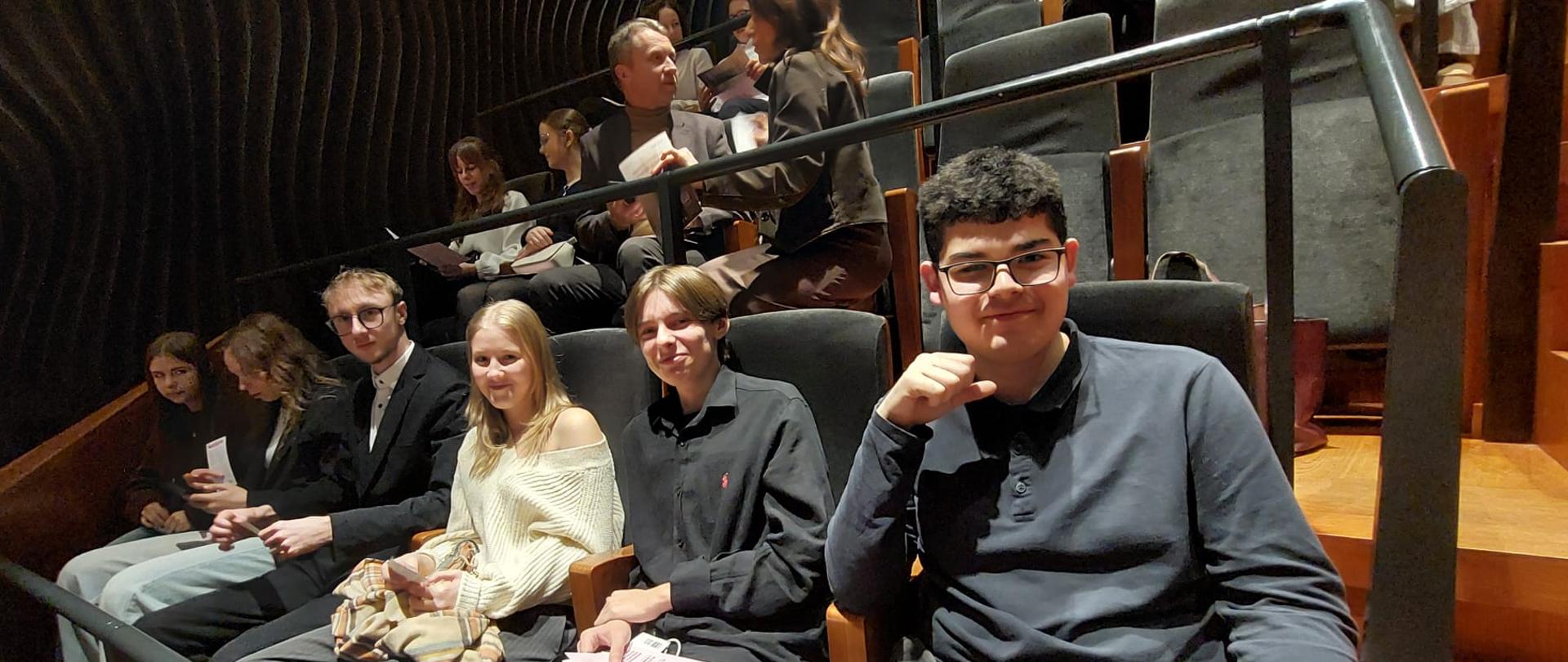 Uczniowie i nauczyciele siedzą na widowni.