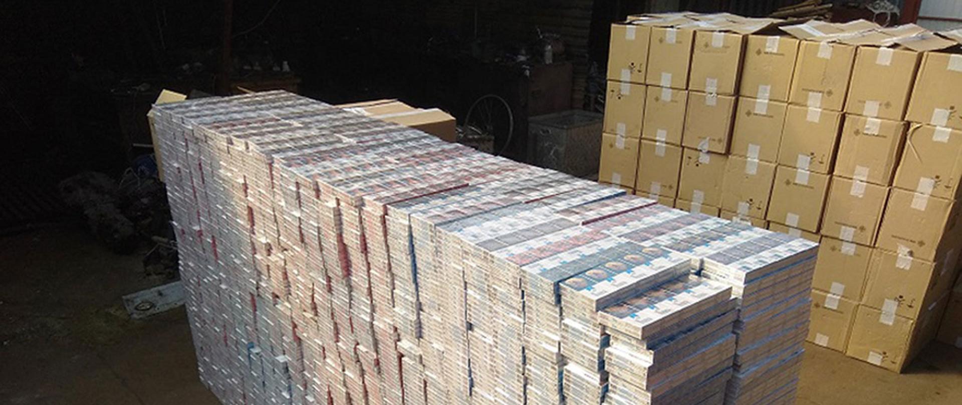 Paczki z papierosami ułożone w dużą stertę, za nimi pudła kartonowe.