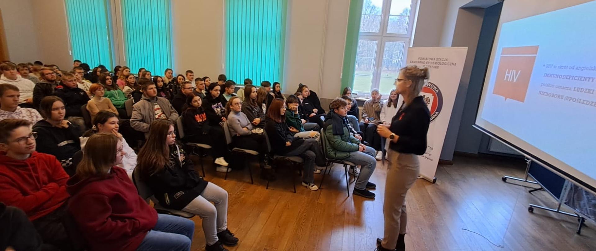 Sala, uczniowie na prelekcji, prelegent, na ekranie wyświetlana prezentacja o tematyce HIV i AIDS