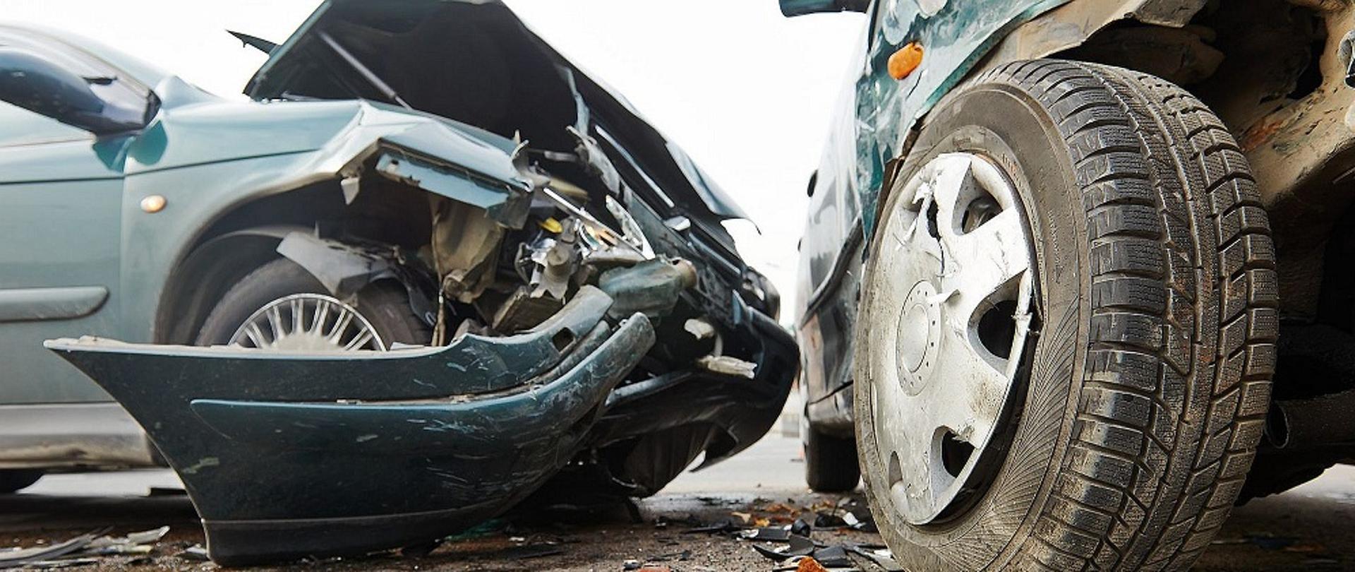 Zdjęcie przedstawia na jasnym tle dwa uszkodzone samochody osobowe po wypadku drogowym