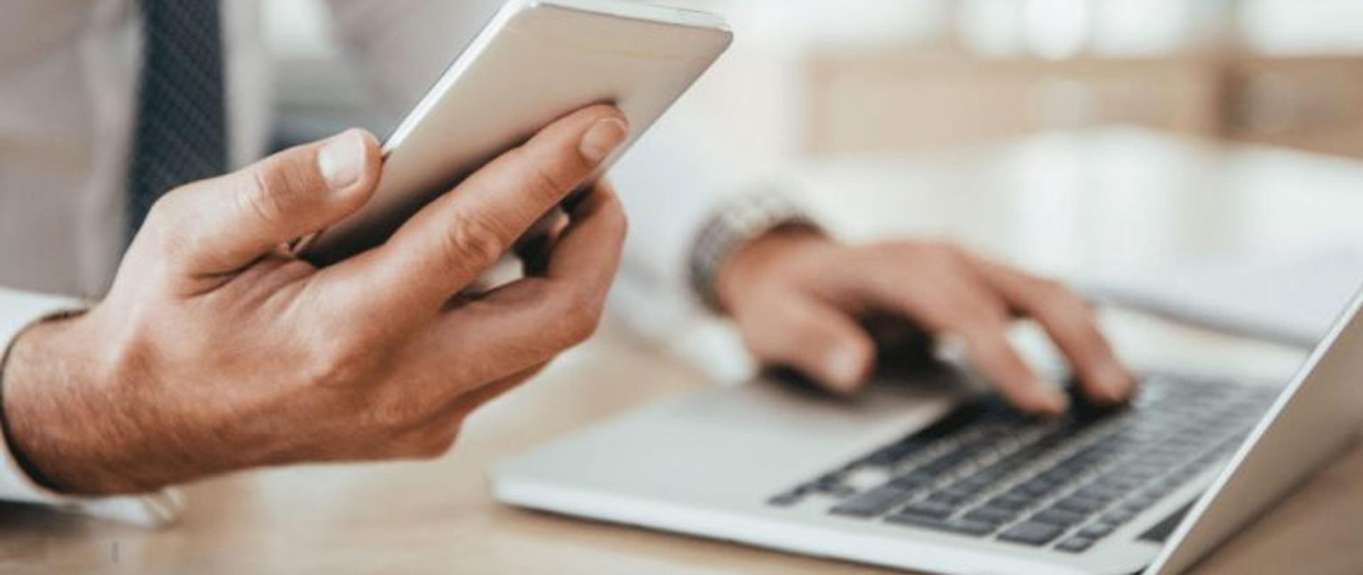 Telefon komórkowy i laptop obsługiwany męską dłonią