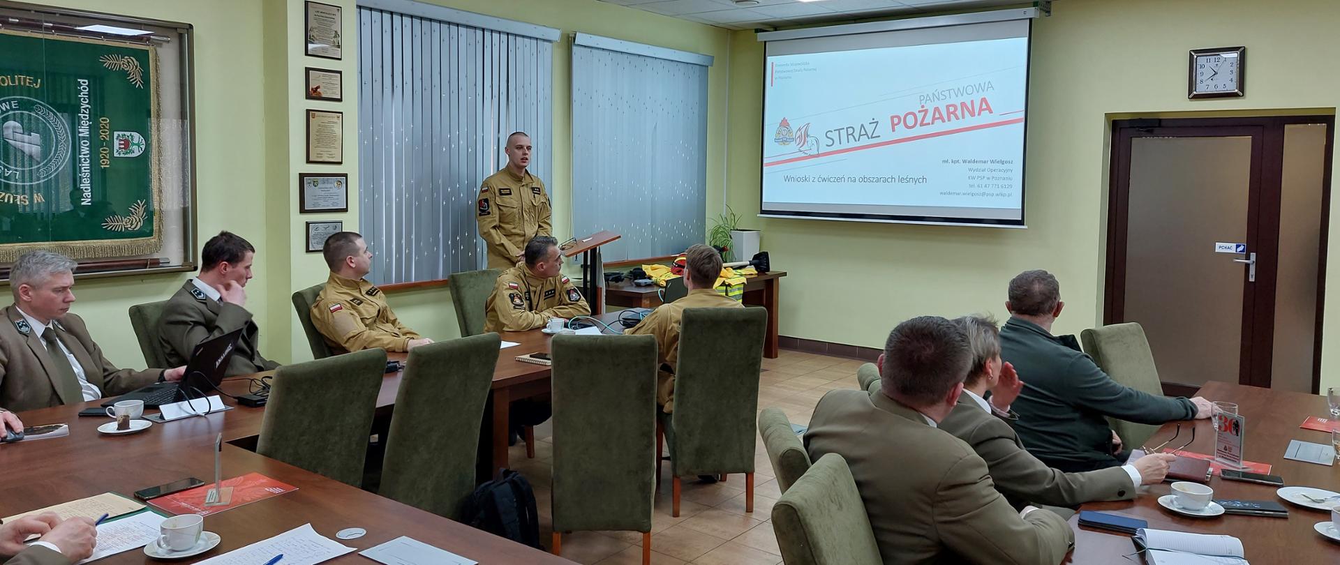przy stołach siedzą leśnicy oraz strażacy, szkolenie, przed nimi duży ekran ze slajdem prezentacji 