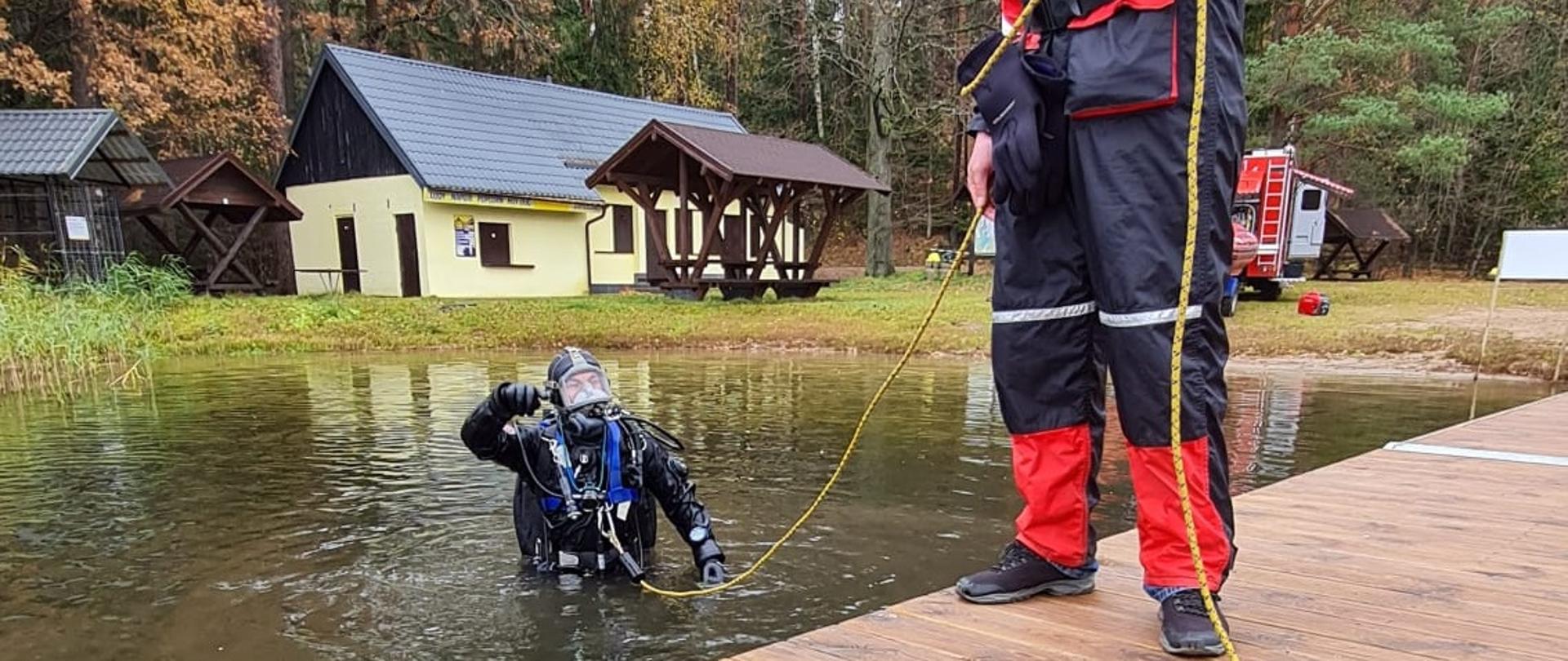 Zdjęcie obrazuje nurka wchodzącego do wody w tle budynki.