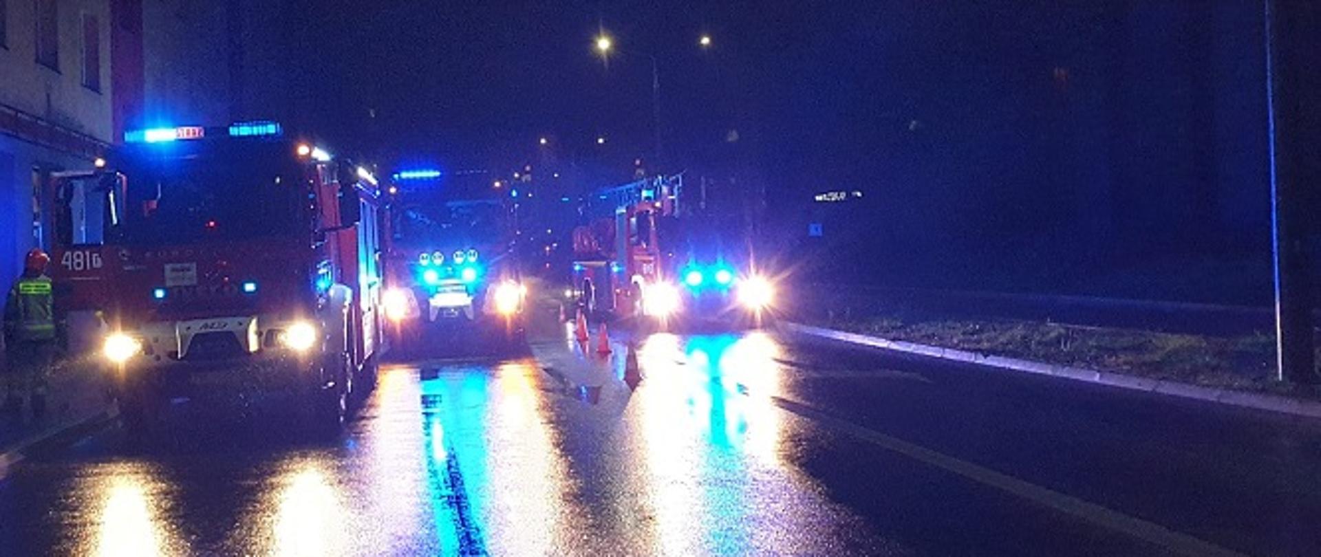 Zdjęcie obrazuje samochody jednostki ratowniczo-gaśniczej ze Skarżyska-Kamiennej stojące na ulicy przy bloku wielorodzinnym w którym gaszono pożar mieszkania.