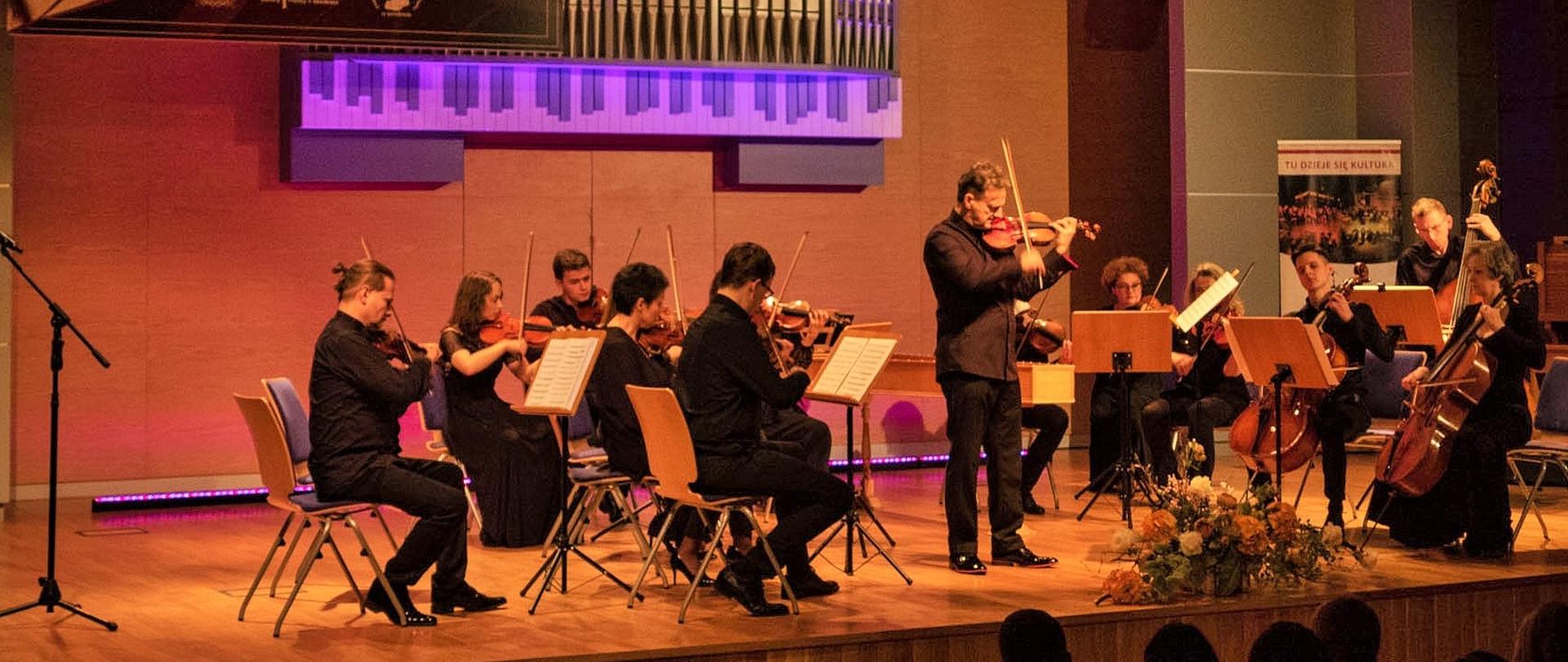 Zdjęcie wykonane w balkonu - ujęcie grającego na skrzypcach artysty, przed nim pulpit z nutami, za nim klawesyn oraz towarzysząca mu orkiestra