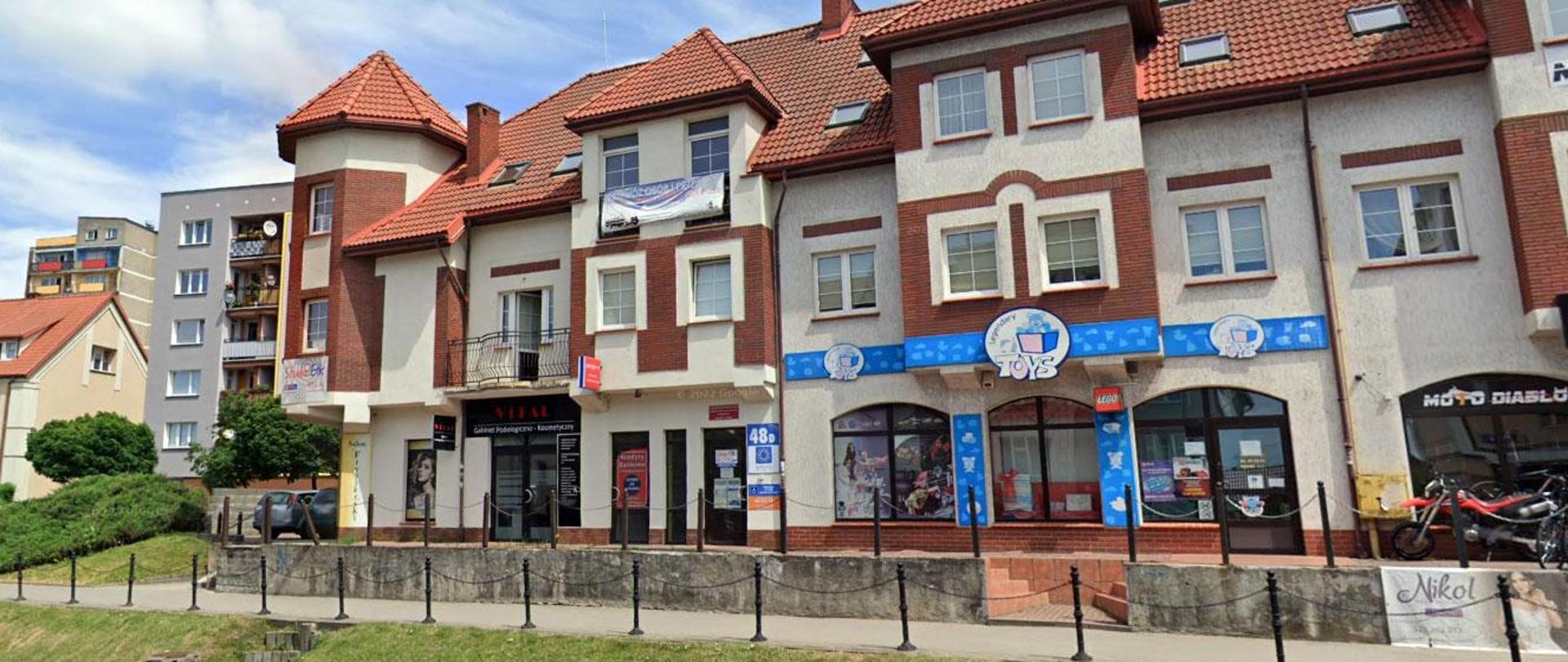 Dwupiętrowy budynek usługowy z czerwonym dachem i jasną elewacją