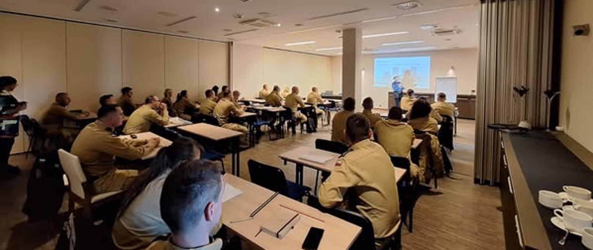 Grupa osób siedzących przy stołach w sali podczas narady służbowej PSP woj. zachodniopomorskiego