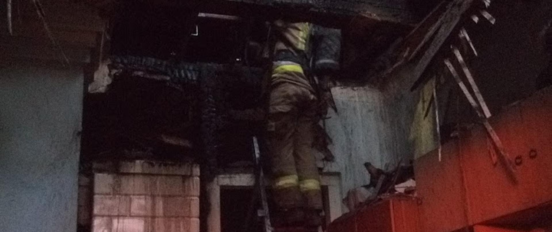 Zdjęcie przedstawia strażaków na drabinie wewnątrz budynku podczas dogaszania pożaru budynku 