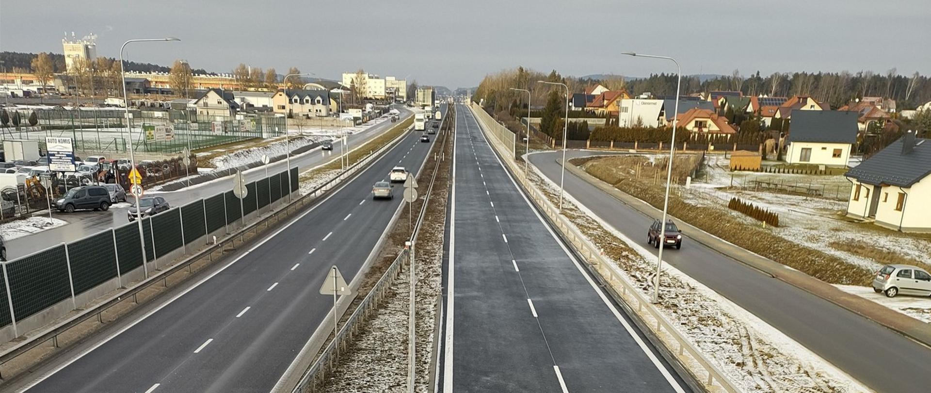 DK73 obwodnica Morawicy - w środku zdjęcia dwujezdniowa droga asfaltowa, po bokach ekrany, drogi dojazdowe, zabudowania 