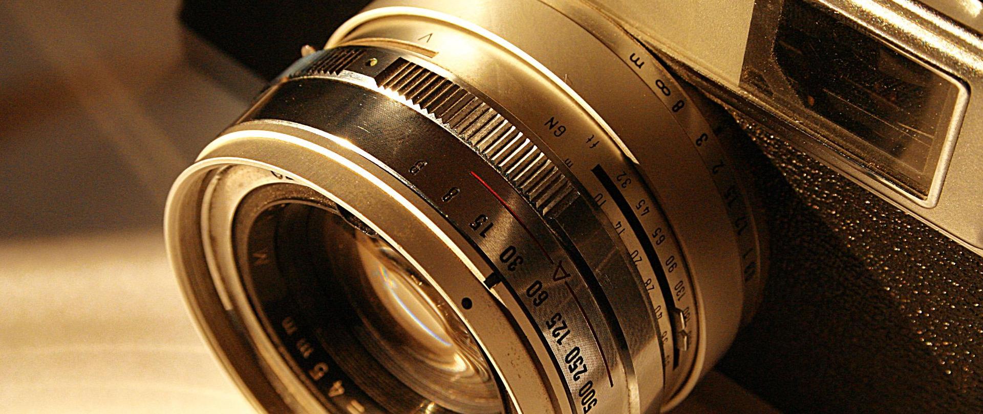 Na zdjęciu aparat fotograficzny, w centralnym miejscu zdjęcia obiektyw.