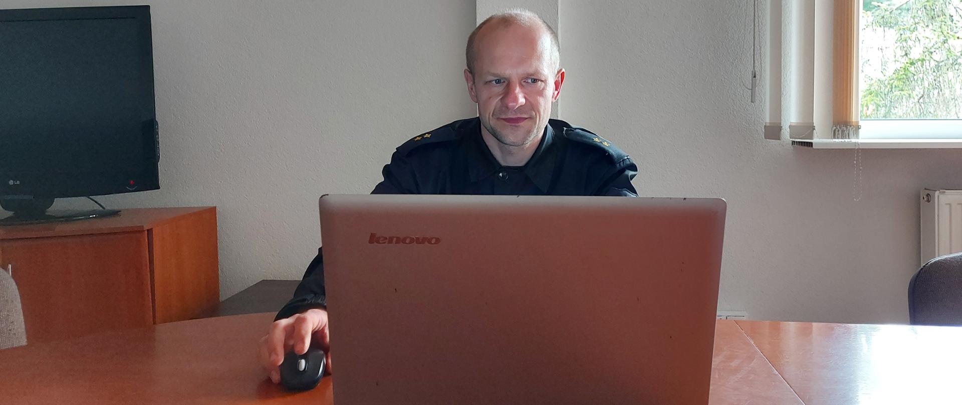 Zdjęcie ilustracyjne do szkolenia seniorów. Na zdjęciu widać strażaka przed laptopem. 