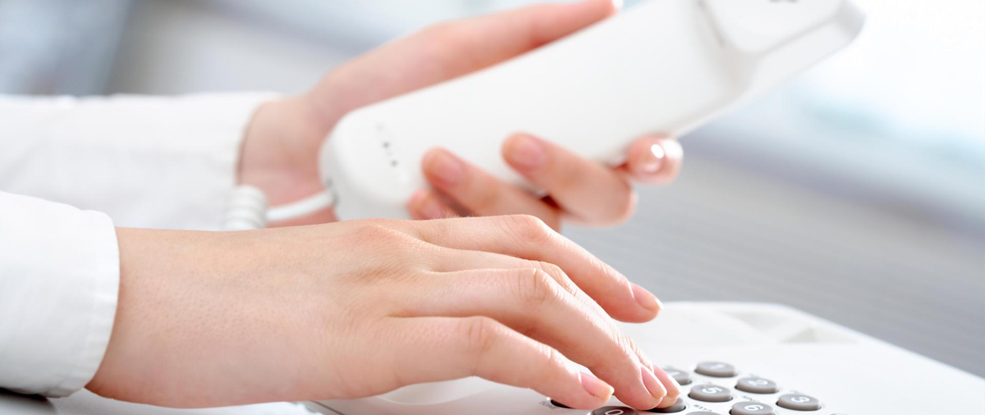W lewej ręce trzymana słuchawka telefonu a palce prawej ręki naciskają numery na klawiaturze