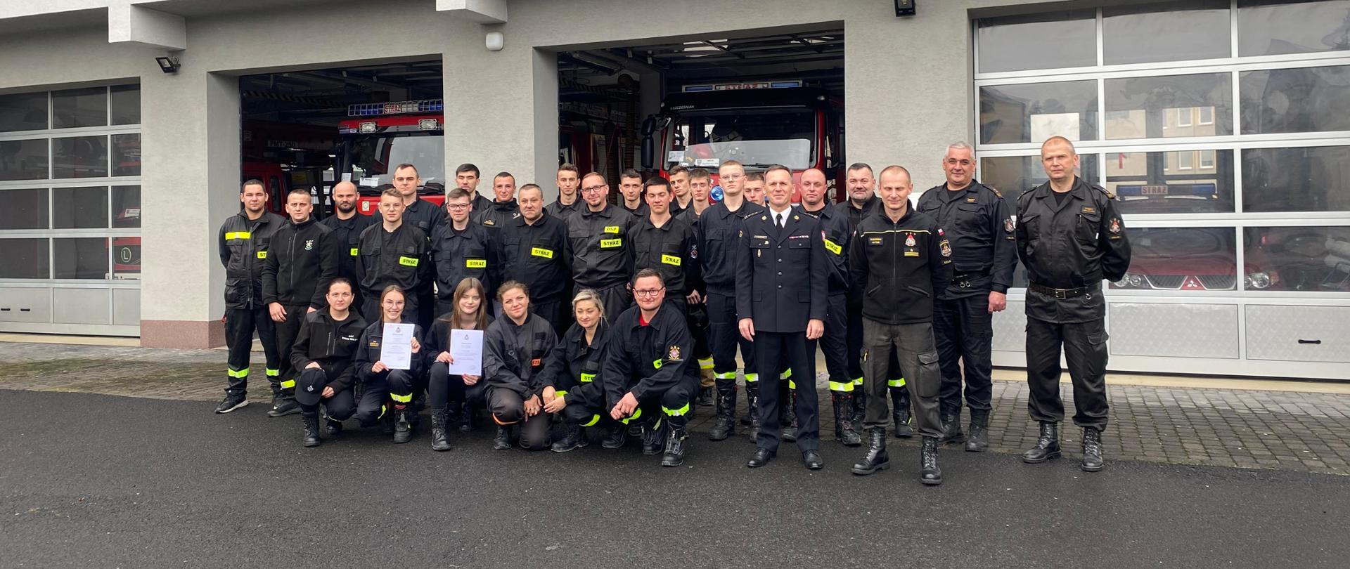 Widzimy jak strażacy OSP wraz z wykładowcami oraz Zastępca Komendanta PSP w Leżajsku pozują do zdjęcia grupowego na tle budynku komendy.