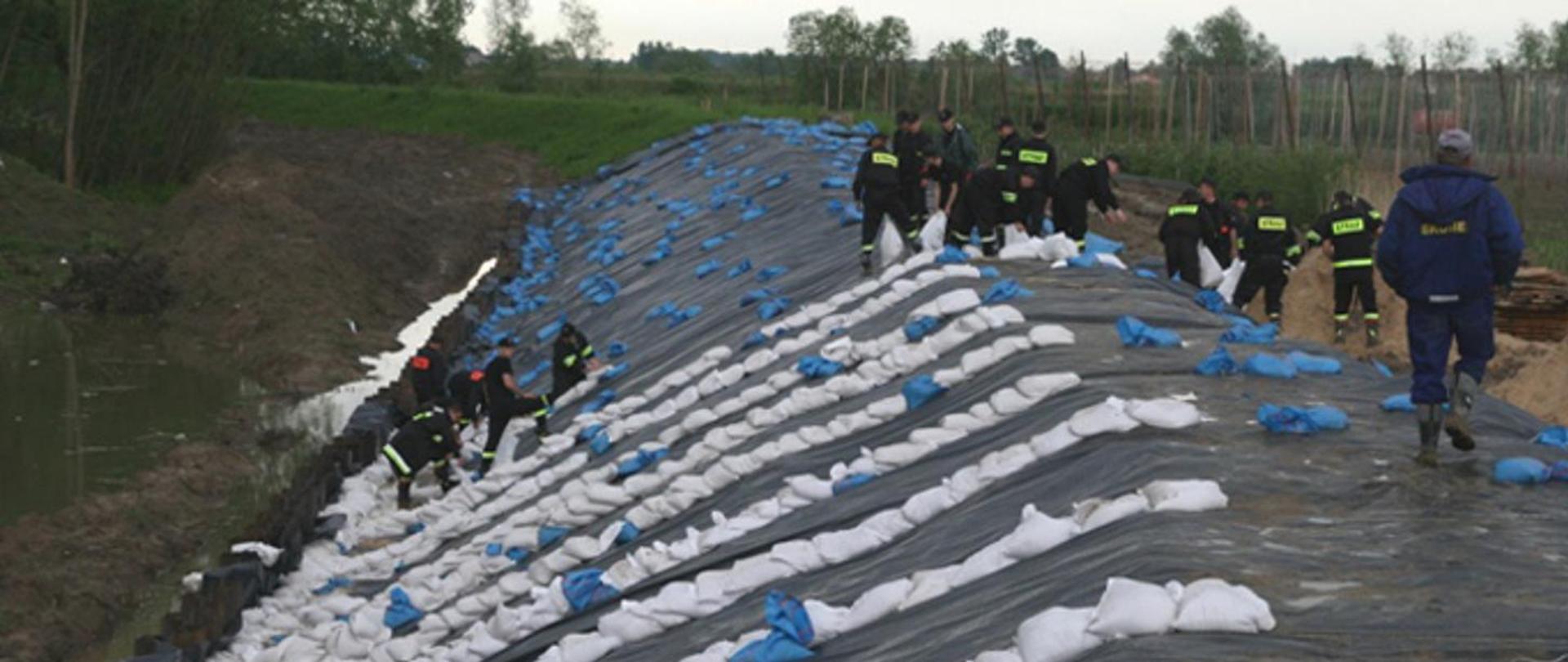 Strażacy przy użyciu foli i worków z piaskiem umacniają wały