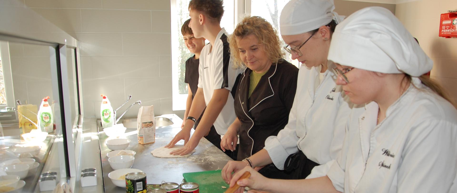 Uczniowie z nauczycilką przy blacie kuchennym przygotowują posiłek