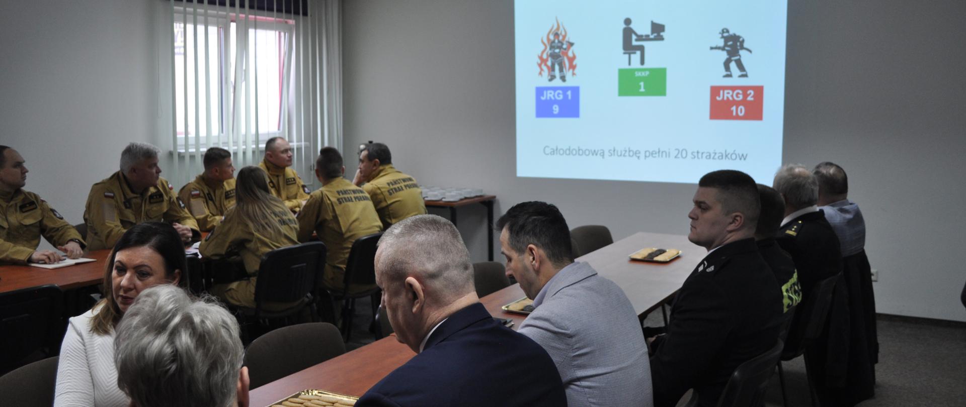 Podczas narady wyświetlana prezentacja, zgromadzeni na sali goście i strażacy