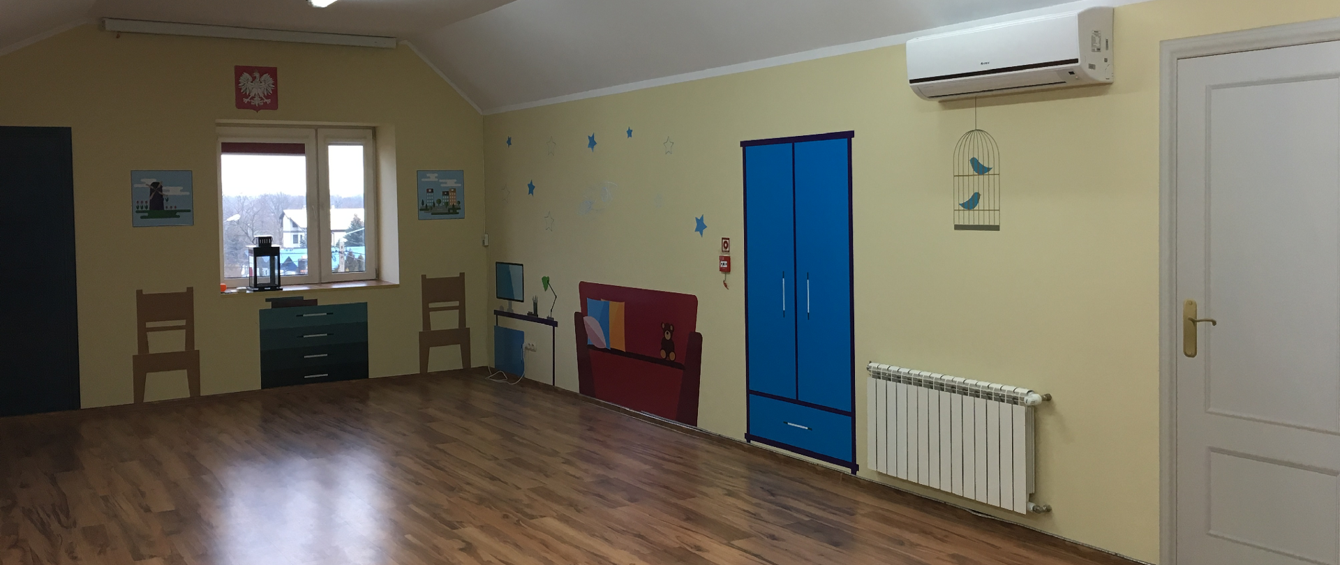 Zdjęcie przedstawia salę edukacyjną, na ścianach naklejki imitujące wyposażenie pomieszczenia w szafę, łóżko itp.