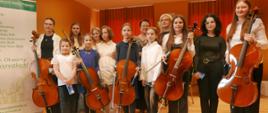 Wspólne klasowe zdjęcie, wszystkie wiolonczelistki z instrumentami razem z nauczycielką i panią akompaniator.