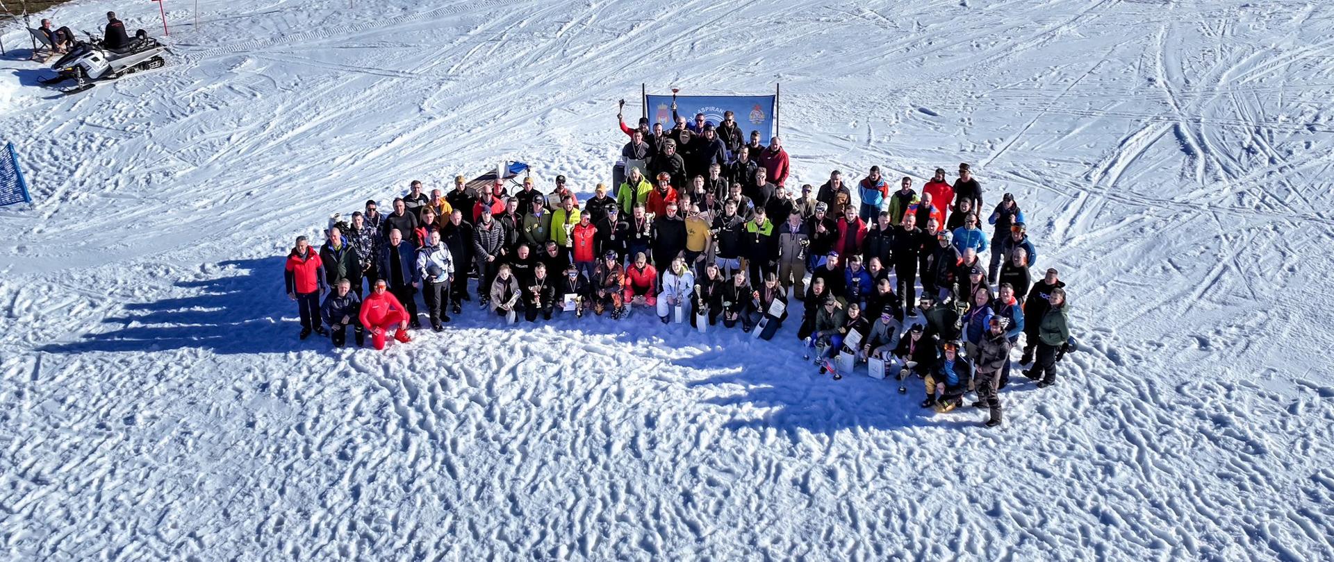 Zdjęcie z drona przedstawiające dużą grupę strażaków i uczestników zawodów zgromadzonych na stoku narciarskim podczas wspólnego zdjęcia po zakończeniu rywalizacji.
