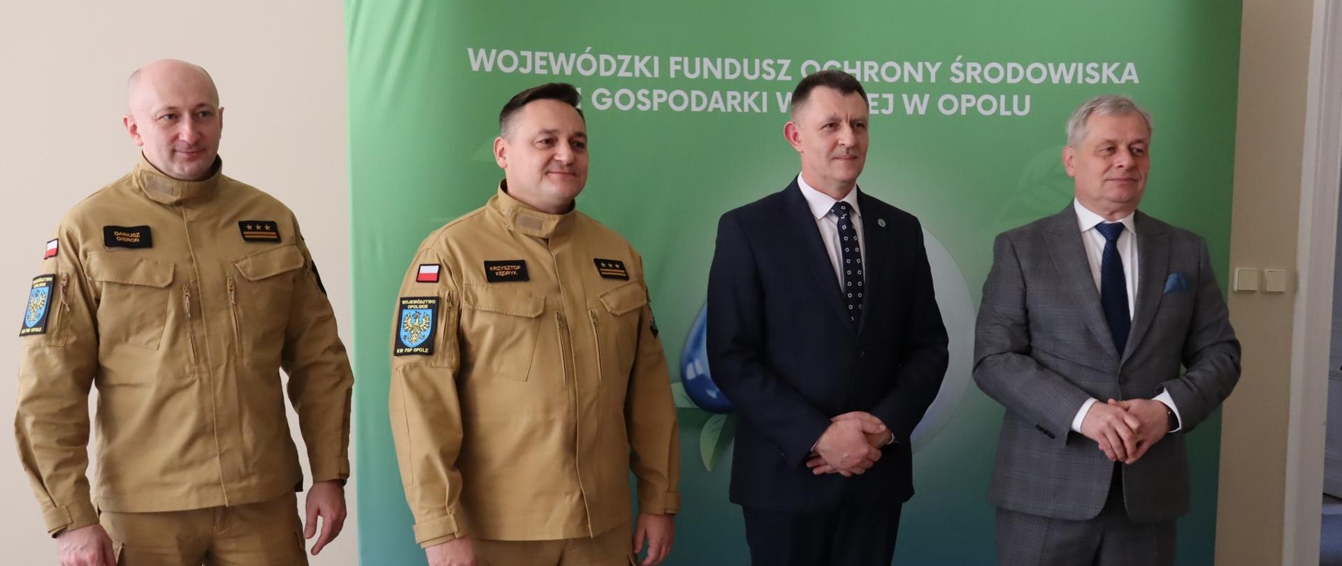 Briefing prasowy w związku z rozpoczęciem programu dofinansowania OSP województwa opolskiego. W briefingu wziął udział Pan Sławomir Kłosowski Wojewoda Opolski, Pan Jerzy Naszkiewicz Zastępca Prezesa Zarządu WFOŚiGW w Opolu, st. bryg. Krzysztof Kędryk Opolski Komendant Wojewódzki PSP oraz st. bryg. Dariusz Gieroń Zastępca Opolskiego Komendanta Wojewódzkiego PSP. Osoby stoją na tle banneru Wojewódzkiego Funduszu Ochrony Środowiska i Gospodarki Wodnej w Opolu.