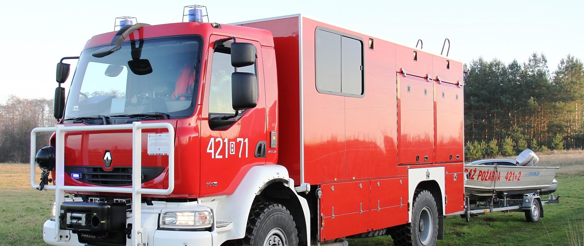 Na zdjęciu samochód ratownictwa wodnego Renault Midlum – SRW z podczepioną łodzią aluminiową. Pojazdy stoją na brzegu kanału przy miejskiej oczyszczalni ścieków. W tle las.