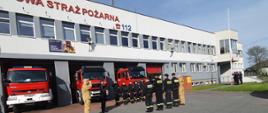 Zdjęcie przedstawia funkcjonariuszy stojących w szyku przed budynkiem KP PSP w Opatowie. Funkcjonariusze oddają honory podczas podnoszenia flagi państwowej.
