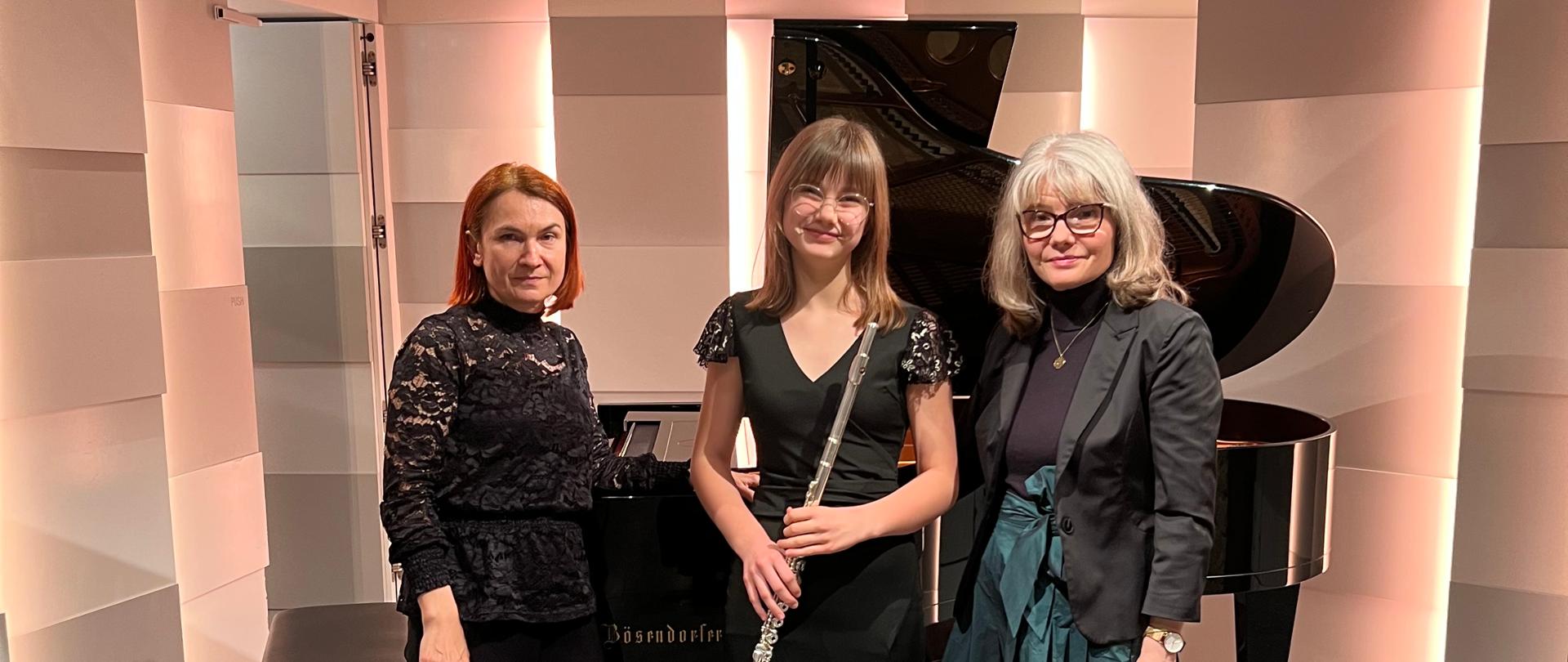 Uczennica ZPSM podczas konkursu, z nauczycielami, na tle fortepianu