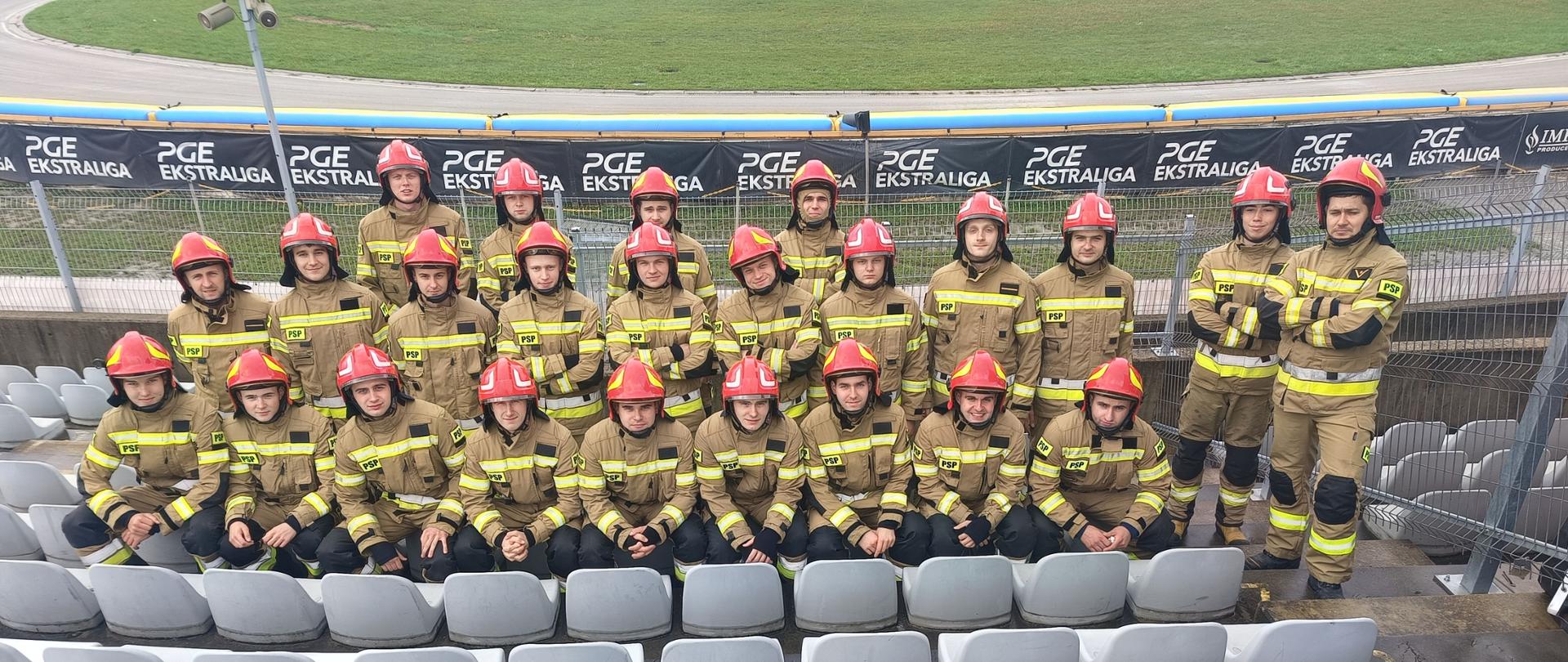 Strażacy Centralnej Szkoły PSP w umundurowaniu bojowym na pamiątkowym zdjęciu na trybunie stadionu żużlowego
