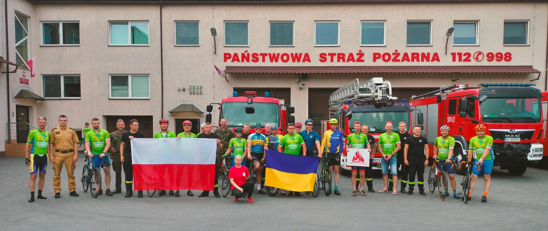 Zdjęcie kolarzy z funkcjonariuszami JRG Zambrów na tle samochodów pożarniczych.