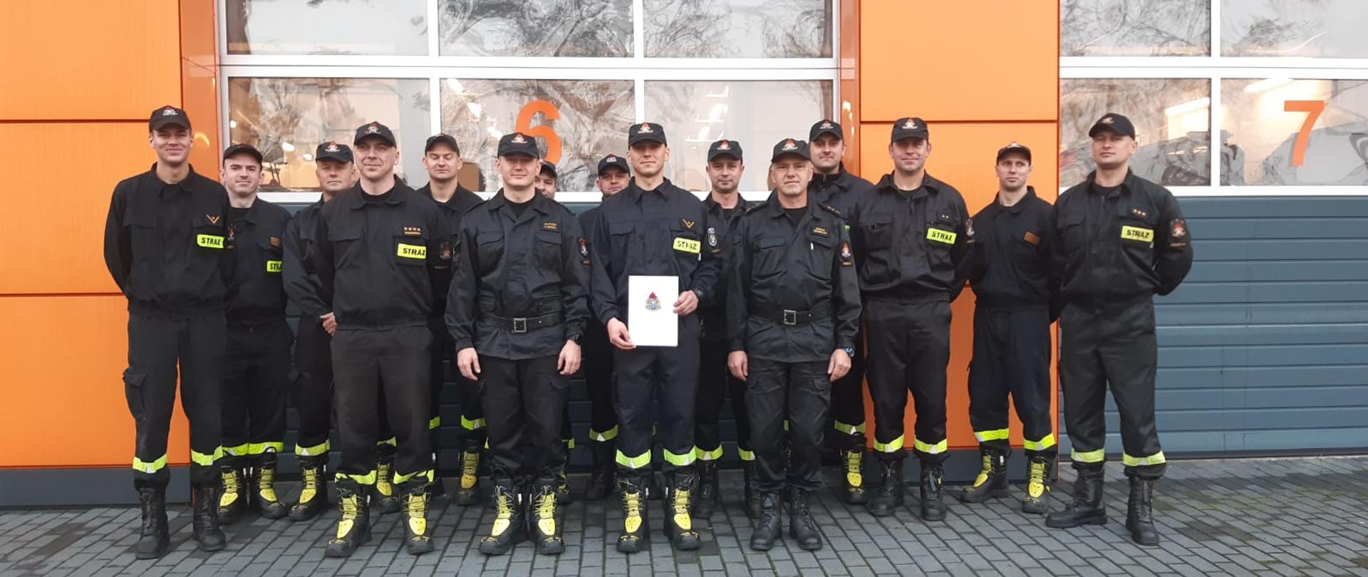 Zdjęcie przedstawia grupę strażaków. Pośrodku stoi strażak awansowany na wyższe stanowisko służbowe.