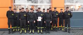Zdjęcie przedstawia grupę strażaków. Pośrodku stoi strażak awansowany na wyższe stanowisko służbowe.
