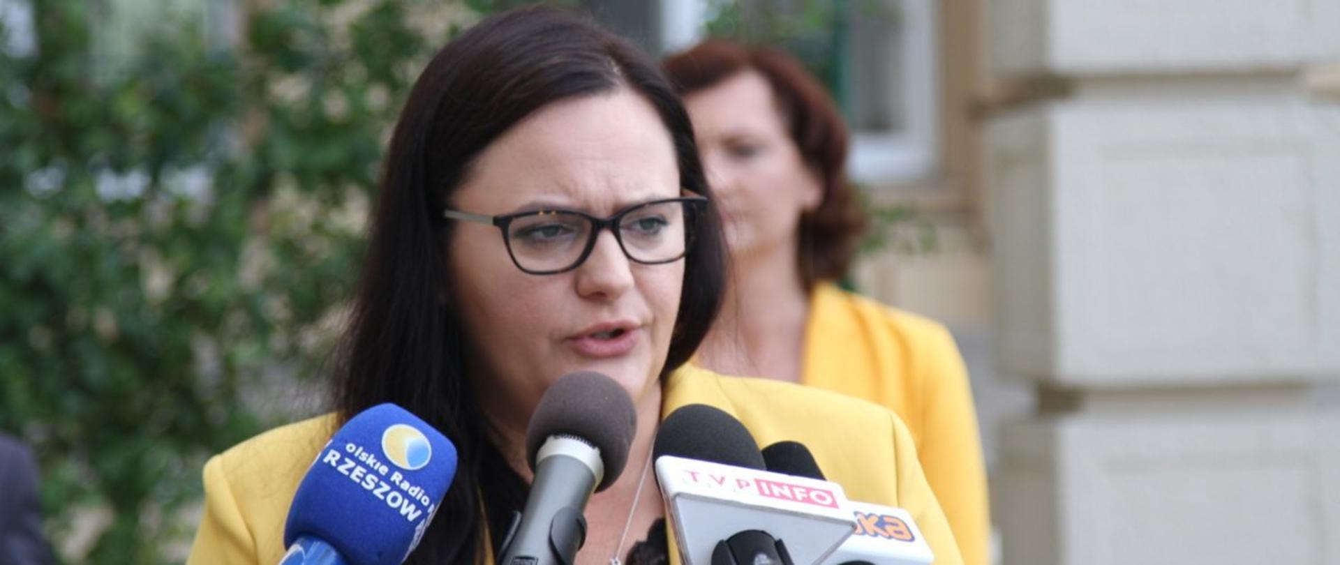 Zdjęcie w plenerze. Małgorzata Jarosińska-Jedynak mówi do mikrofonów.