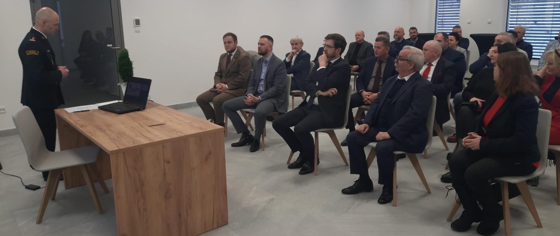 Komendant miejski państwowej straży pożarnej w Elblągu stoi na przeciwko zaproszonych gości. 