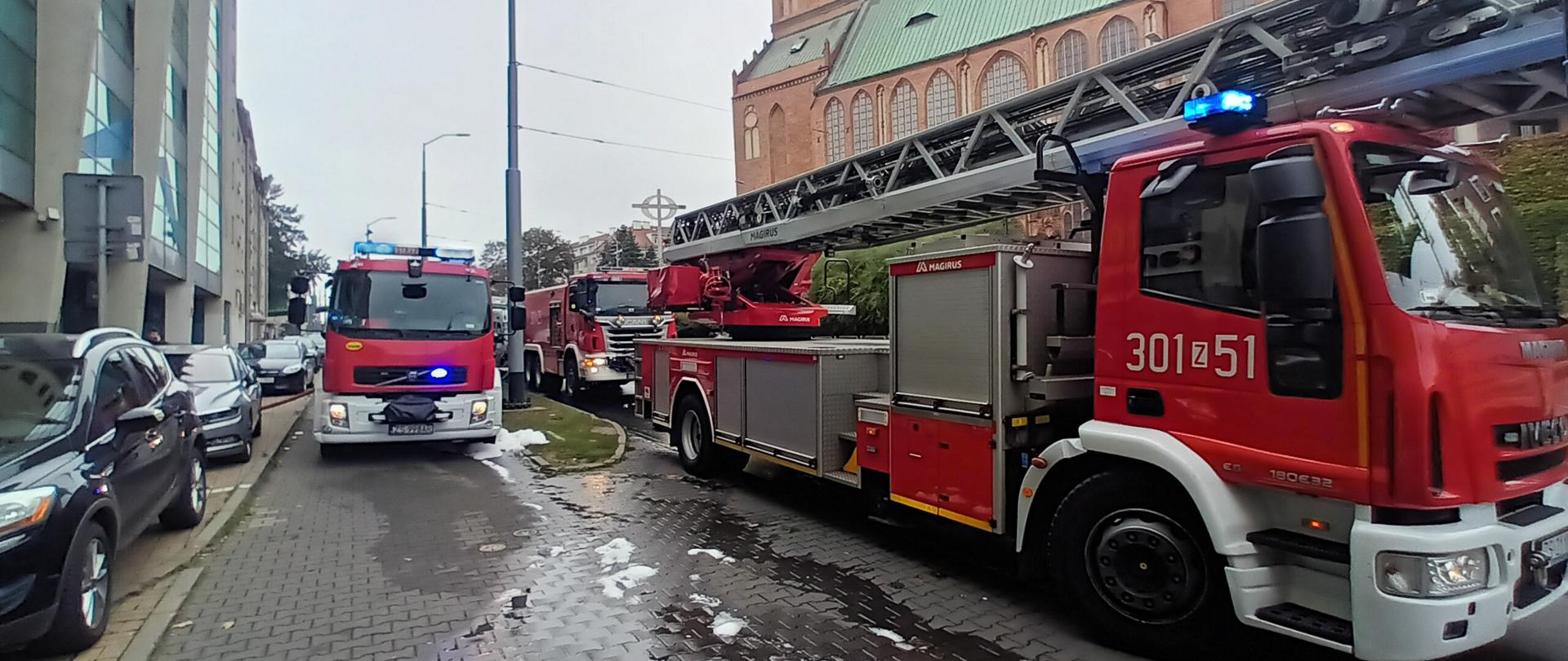 Na ulicy Wyszyńskiego widoczne trzy samochody straży pożarnej w tym jeden pojazd z drabiną mechaniczną.