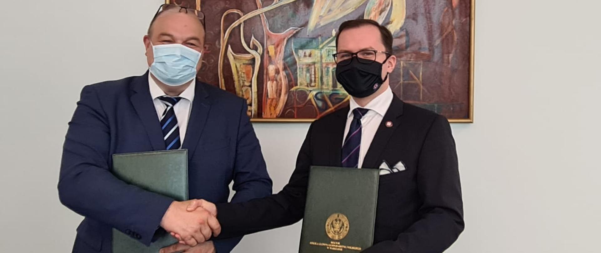 Dwaj mężczyźni w maseczkach trzymają dokumenty o współpracy i dzielą uścisk dłoni