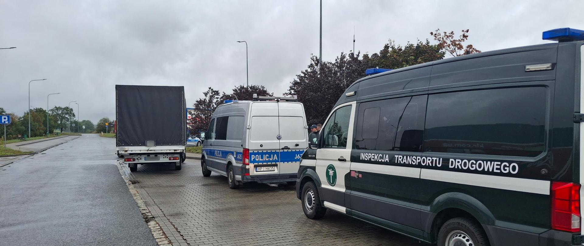 Radiowozy Policji i Inspekcji Transportu Drogowego stojące na parkingu obok zatrzymanego samochodu dostawczego
