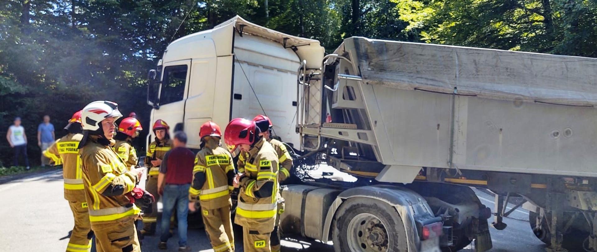 Samochód ciężarowy a obok strażacy.