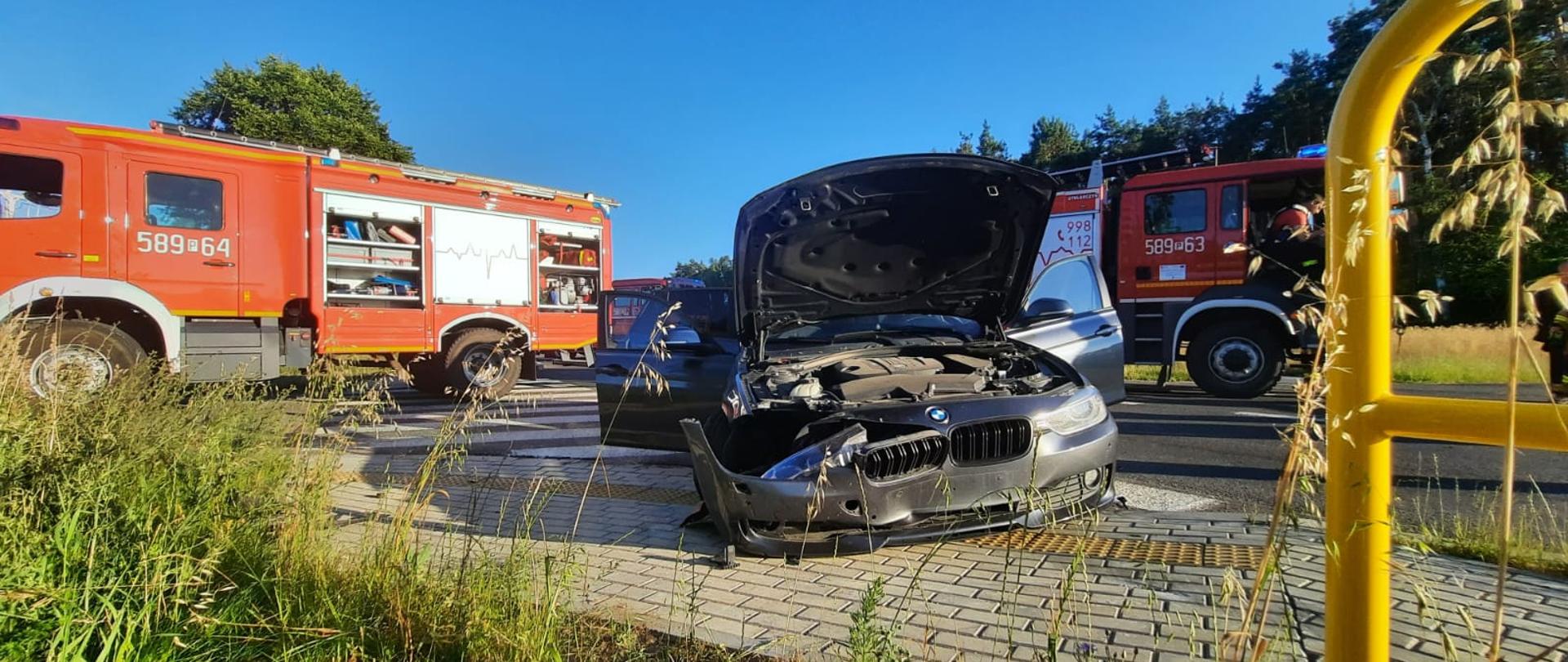 uszkodzony przód samochodu za nim dwa wozy strażackie