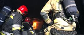 Zdjęcie przedstawia strażaków w trakcie obserwowania rozwoju gaszenia pożaru wewnętrznego i technik jego gaszenia.